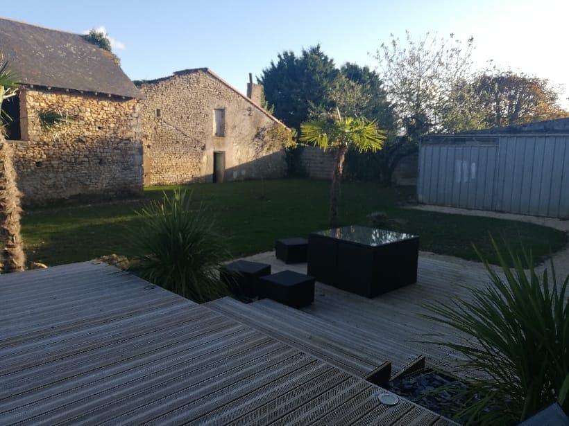 Jardin paysager avec terrasse en bois et grange en pierre, par Artisans de France
