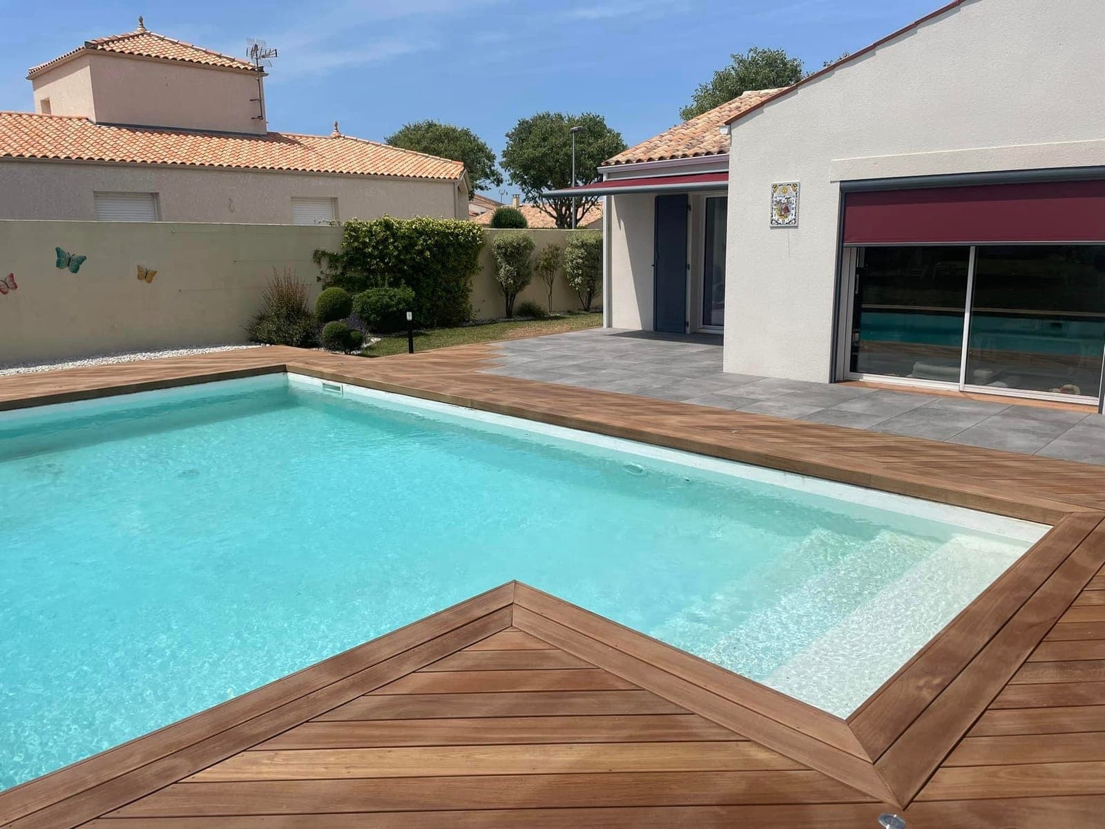 Piscine entourée d'une terrasse en bois et d'un carrelage, réalisée par Artisans de France