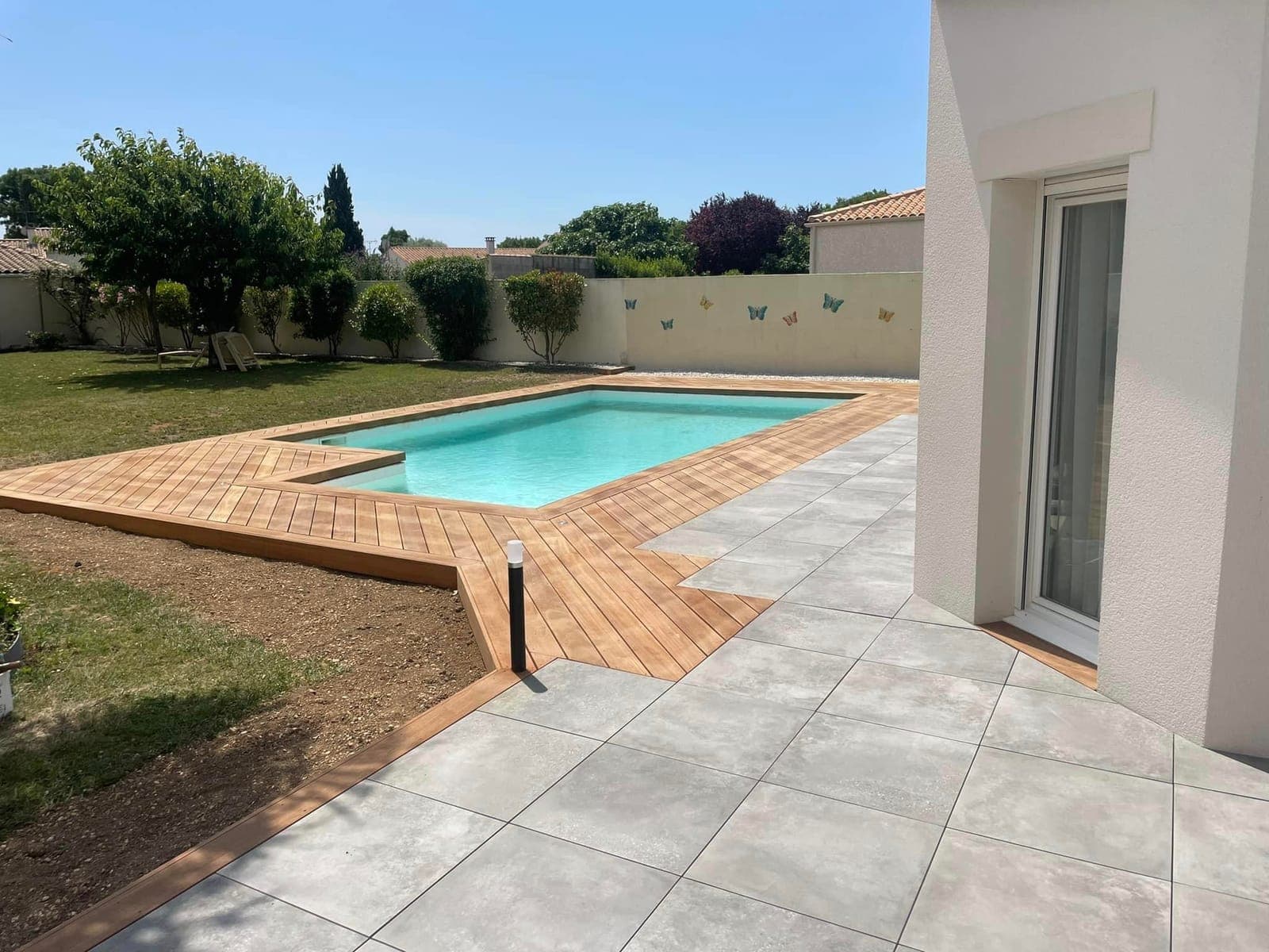Piscine avec terrasse en bois, carrelage et jardin engazonné, par Artisans de France