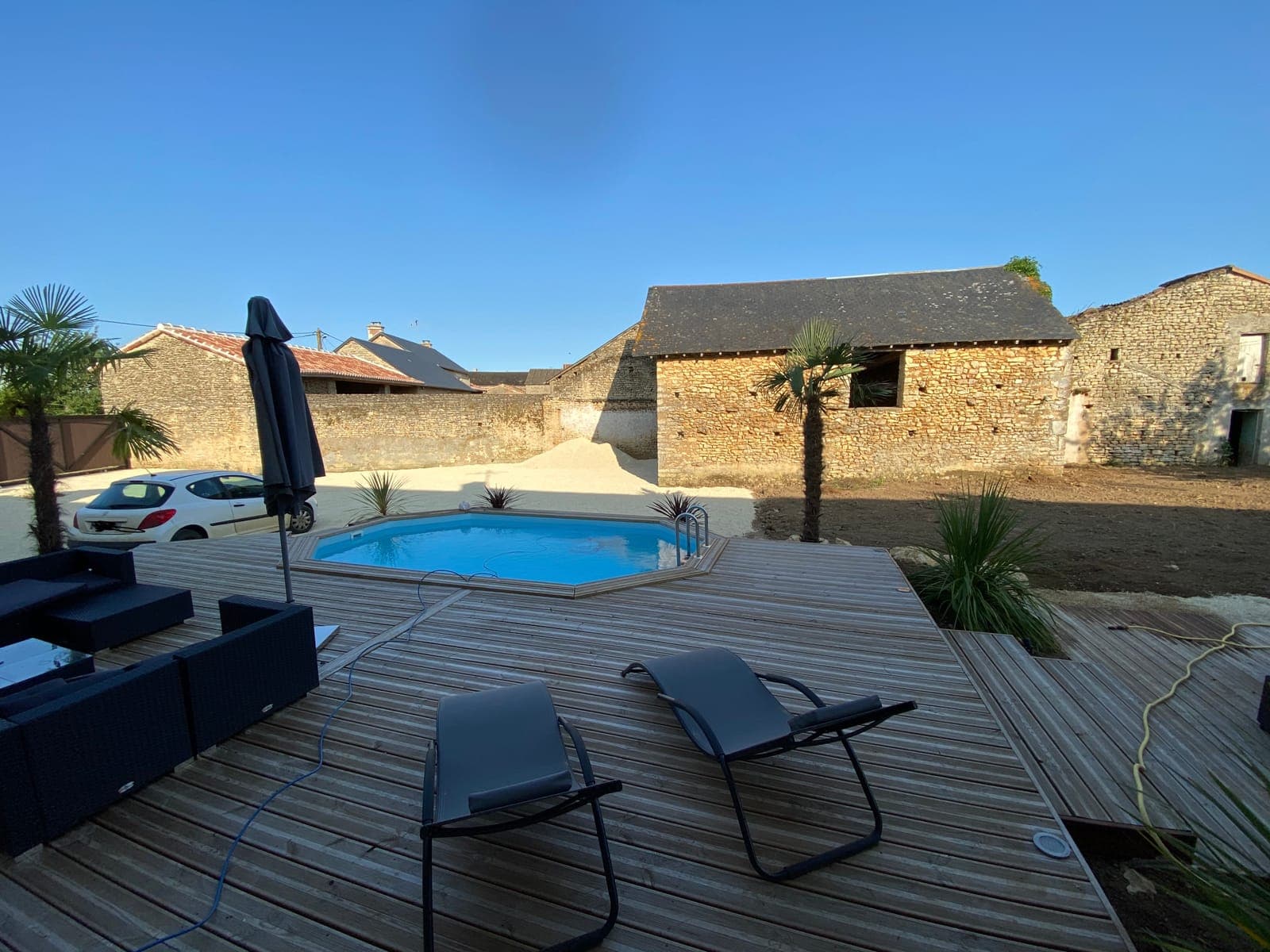 Terrasse en bois et piscine devant une grange en pierre, par Artisans de France